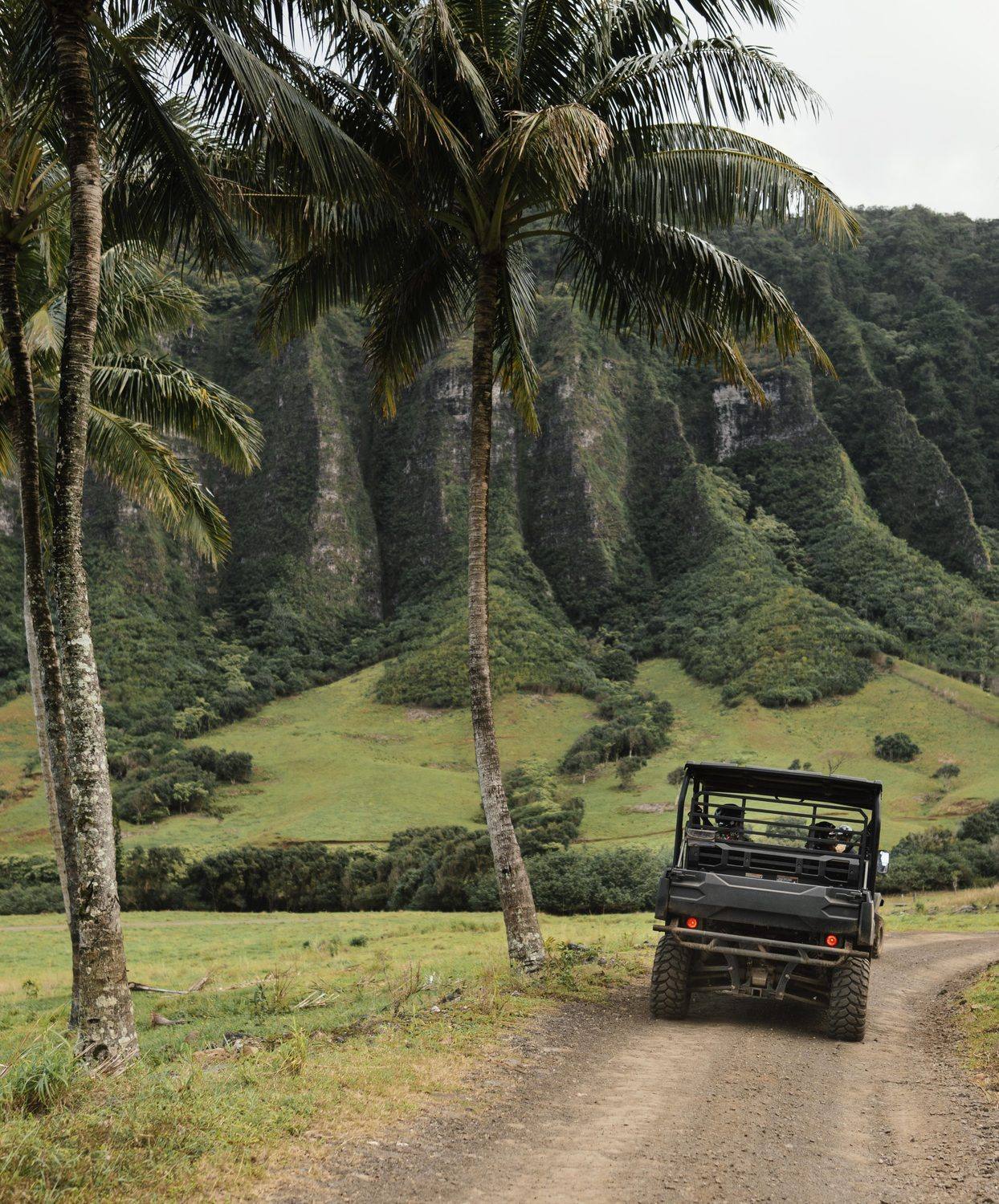 Off-road vehicle on a dirt track below green mountains