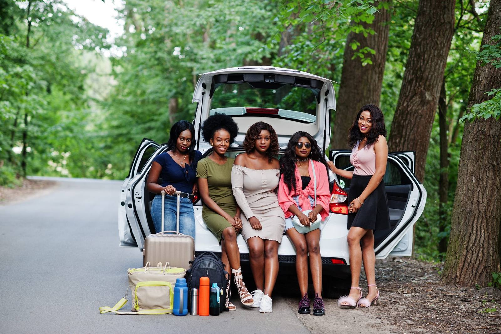Group of friends with bags sitting in the open boot of a car